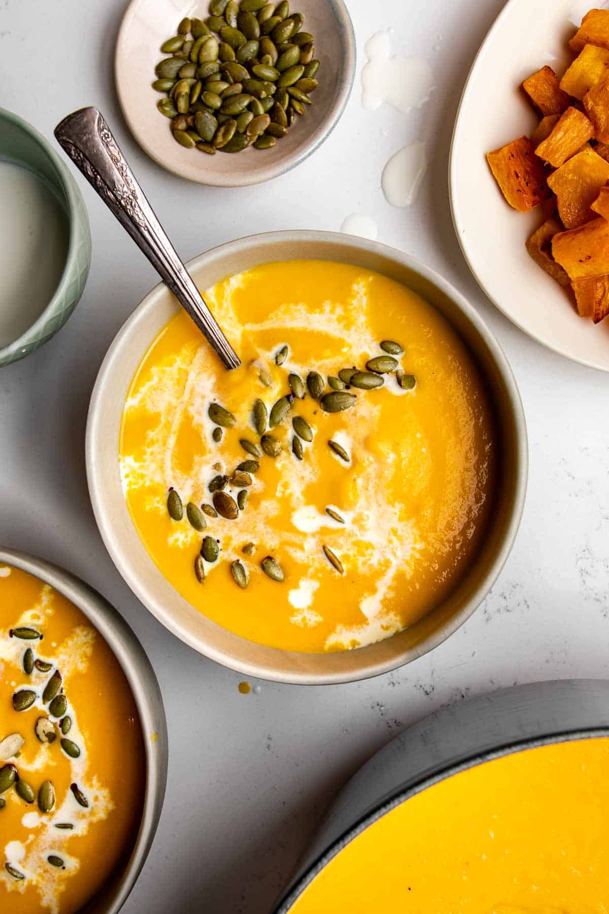 carrot and butternut squash soup in a bowl topped with pumpkin seeds surrounded by ingredients.