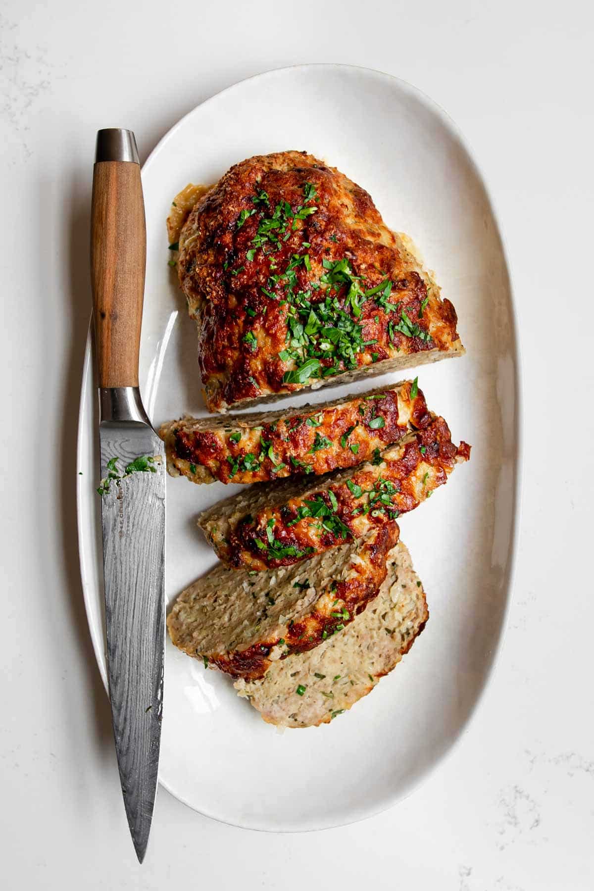 cooked ground chicken meatloaf cut into slices on a serving platter with a knife.
