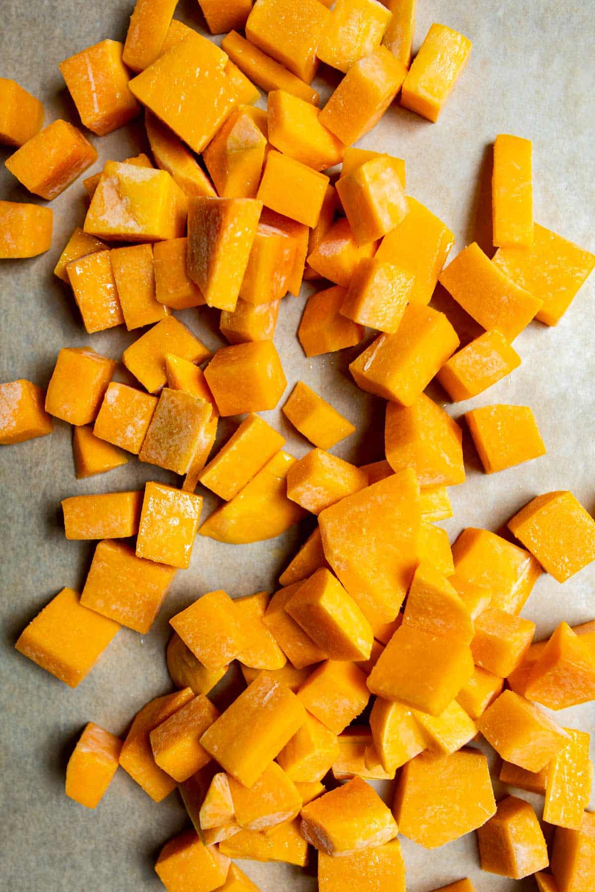 peeled and cubed frozen butternut squash on a sheet pan lined with parchment paper.