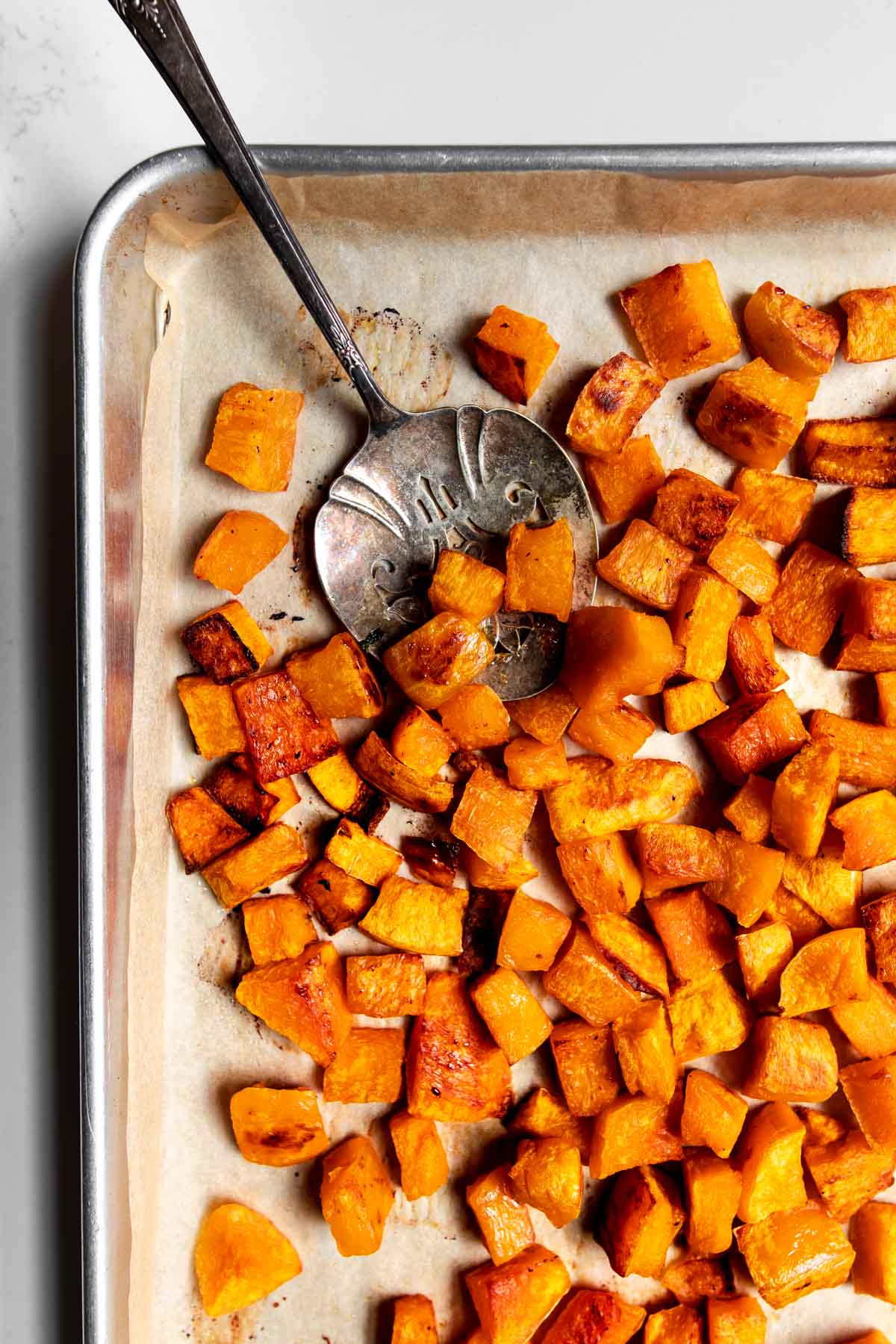 frozen roasted butternut squash on a sheet pan with a serving spoon.