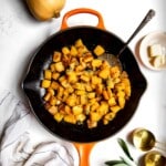 sauteed butternut squash topped with sage in a skillet with a serving spoon.
