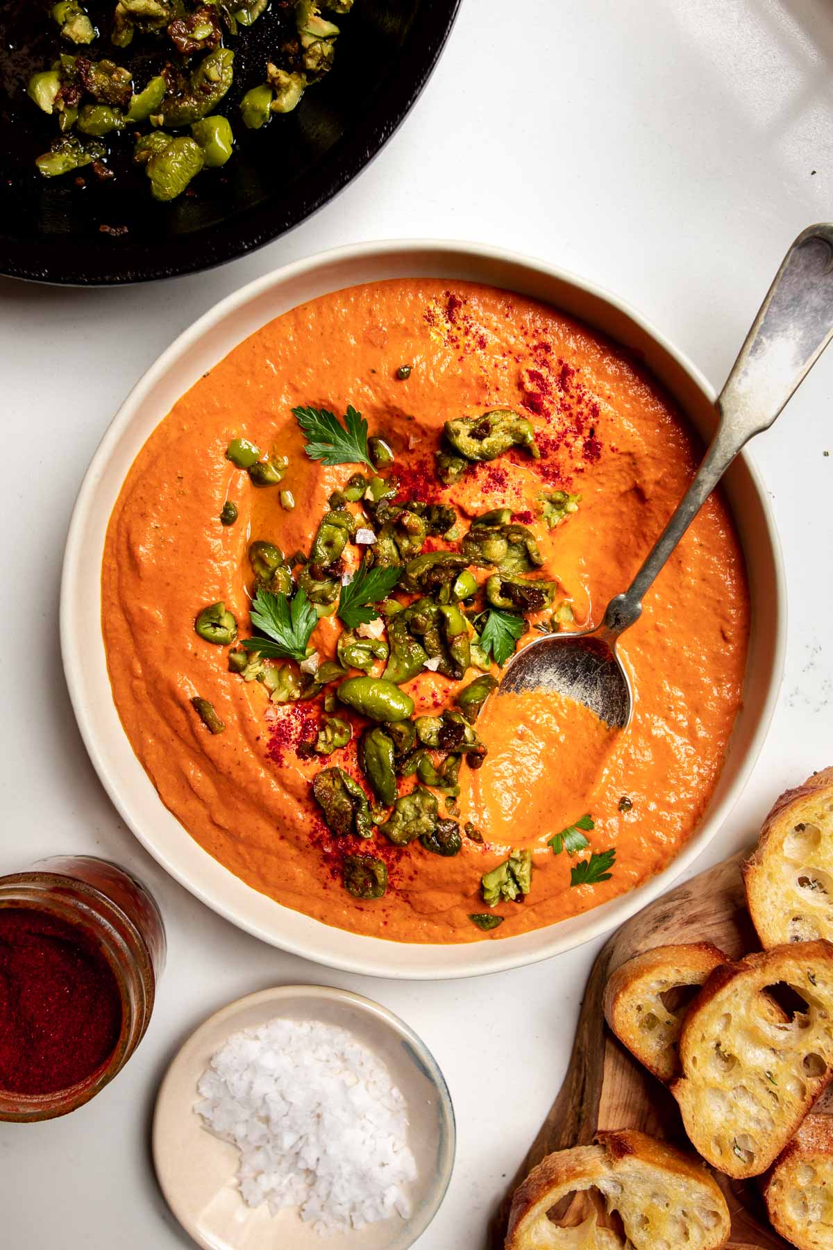 roasted red pepper dip with olives on a plate with a spoon in it and crostini around.