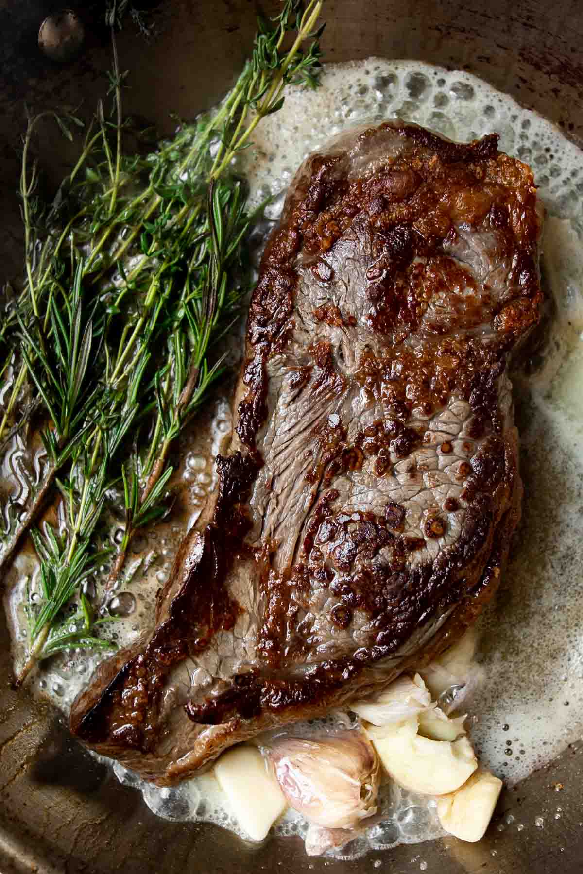 seared steak in a stainless steel pan with garlic, butter and rosemary